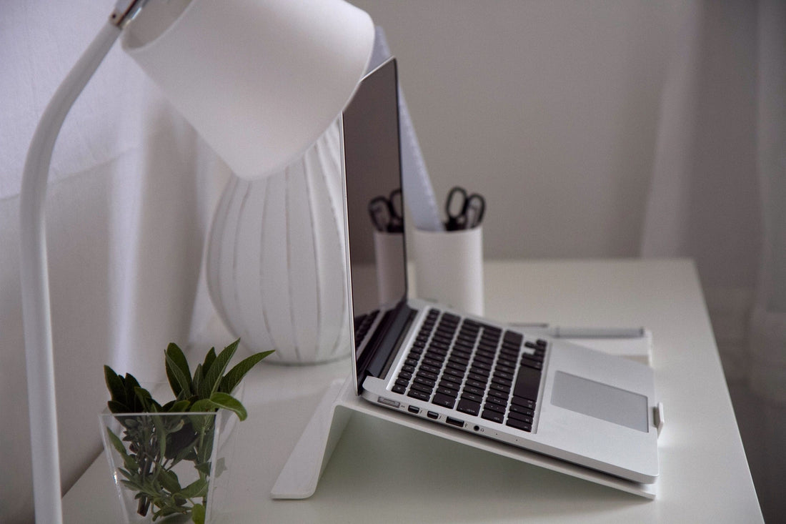 Tidy small white desk with a laptop, desk lamp, pen cup, and a small plant