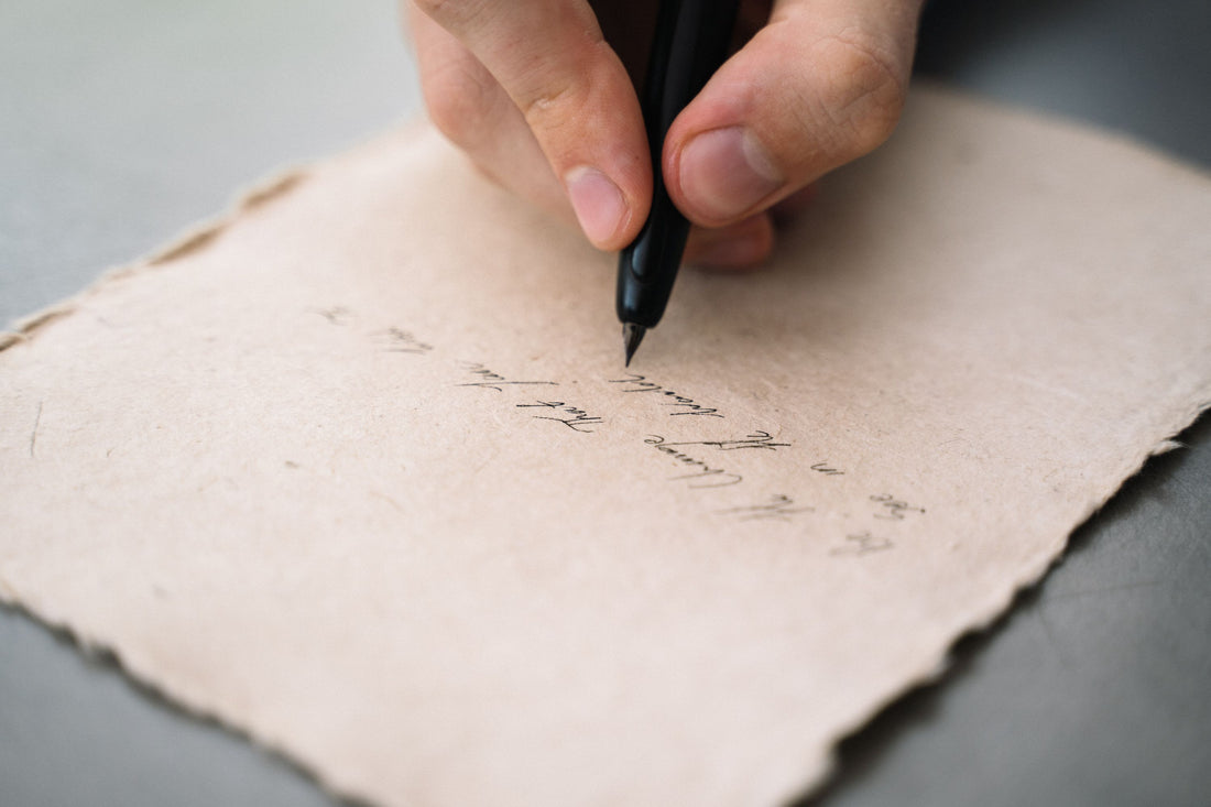 Close-up of a hand writing in cursive with a pen on textured paper