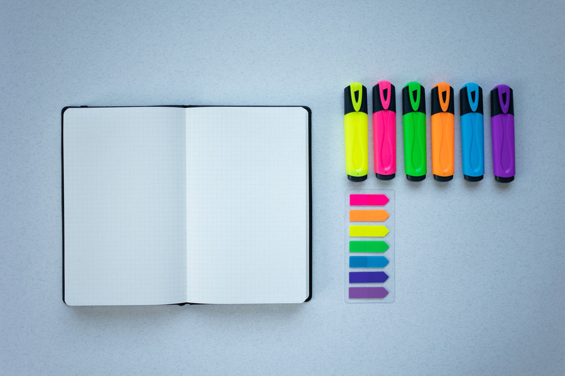 An open notebook next to a lineup of colorful highlighters and page flags