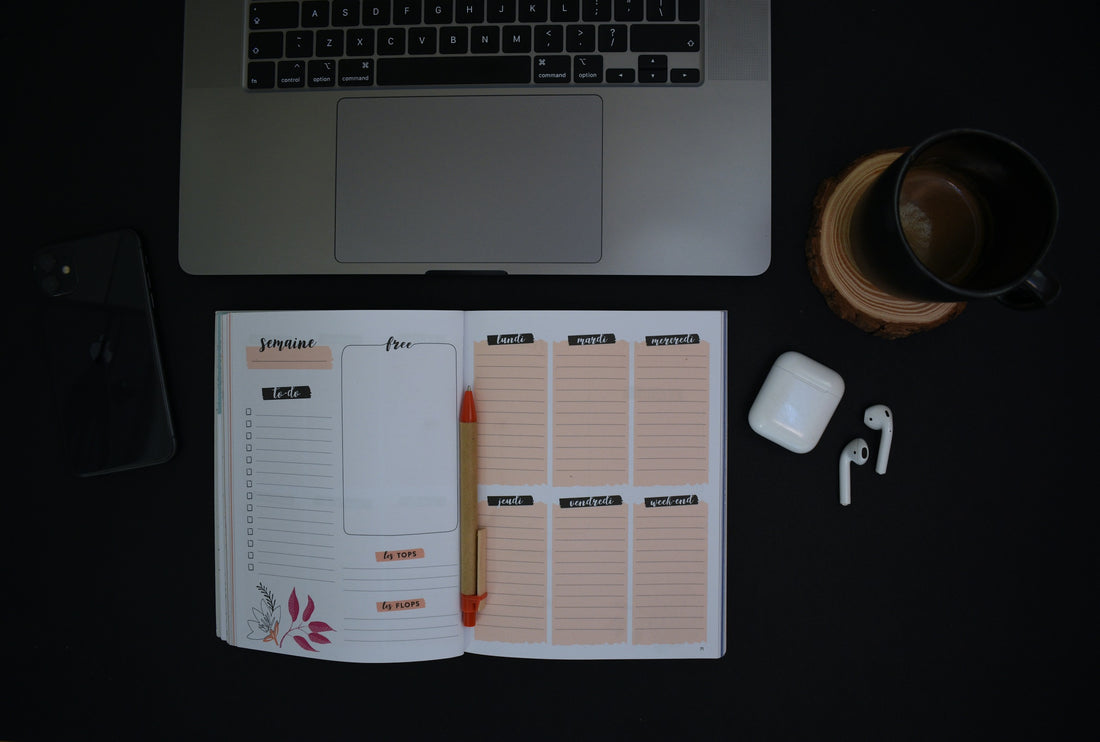Open weekly paper planner next to a laptop, phone, and coffee on a dark desk